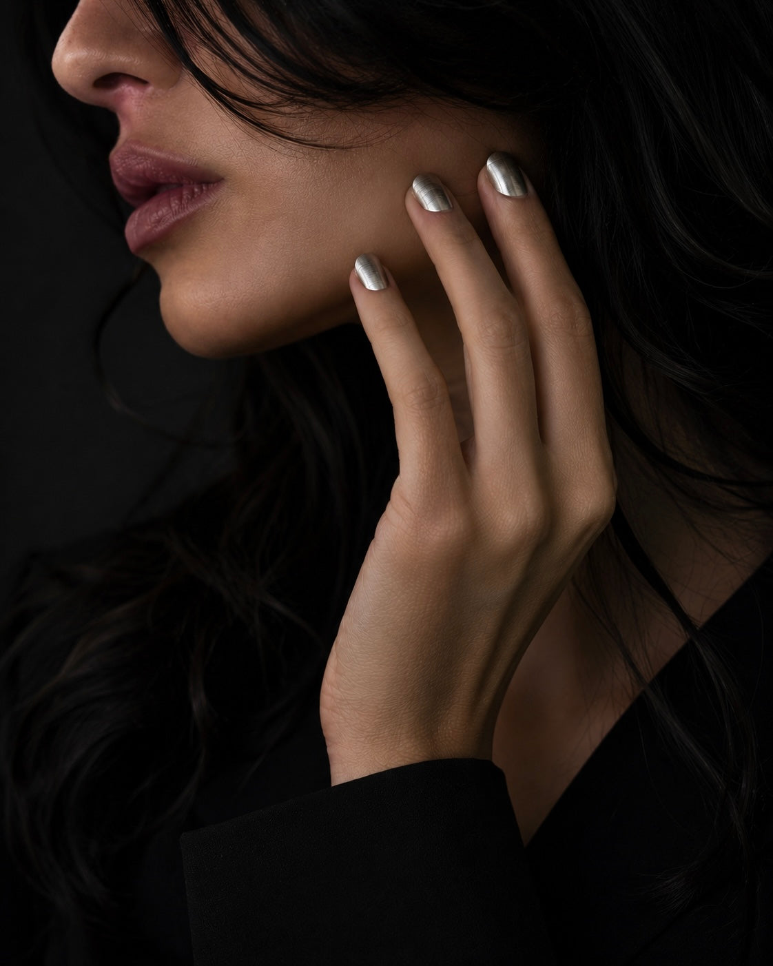 Close-up of a woman's face with hand near her ear against a dark background